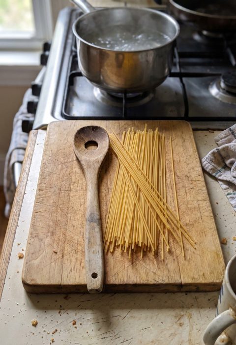 A pasta spoon with a hole in the middle beside dry spaghetti