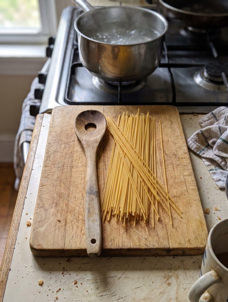 A pasta spoon with a hole in the middle beside dry spaghetti