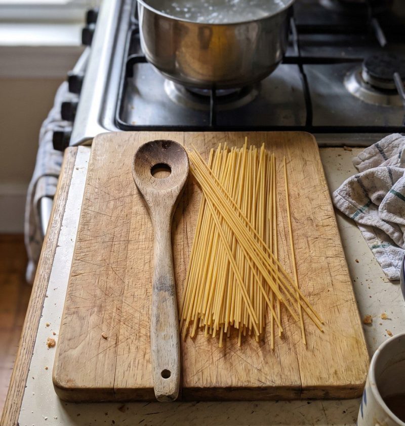 A pasta spoon with a hole in the middle beside dry spaghetti