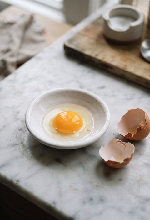 A raw egg yolk in a shallow white dish beside a cracked shell