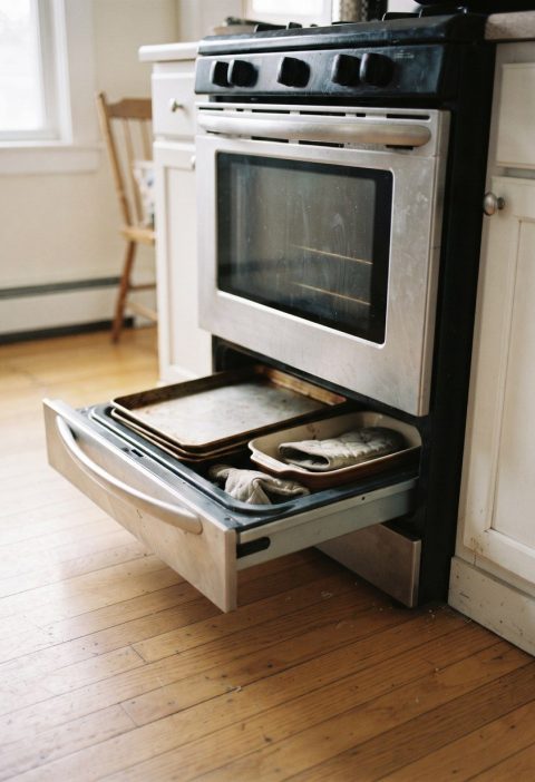 The bottom drawer of an oven standing open with trays inside