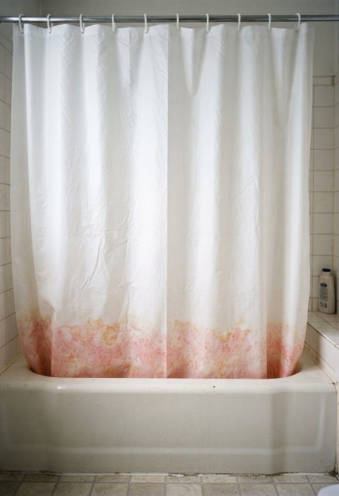A white shower curtain with pink staining along the bottom