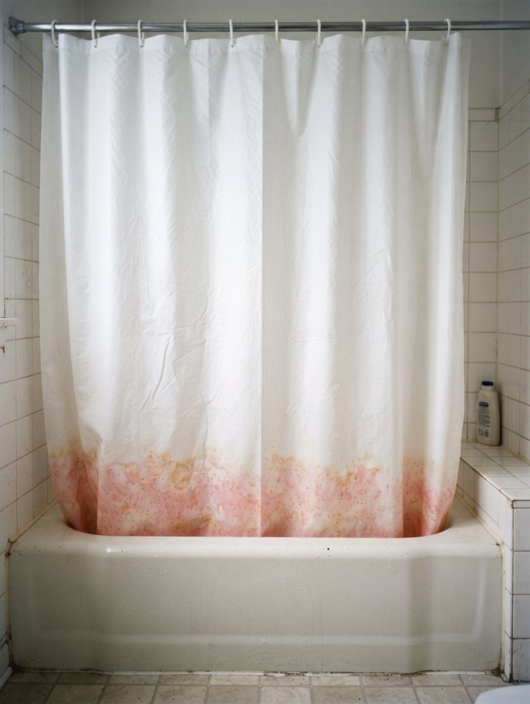 A white shower curtain with pink staining along the bottom