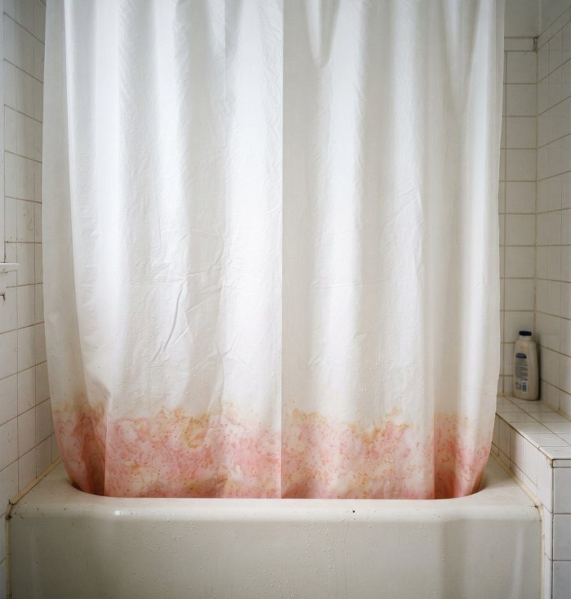 A white shower curtain with pink staining along the bottom