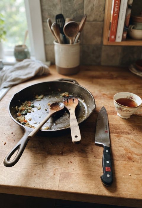 A cast iron skillet, wooden spoons, a knife and a china cup
