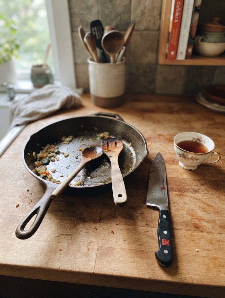 A cast iron skillet, wooden spoons, a knife and a china cup