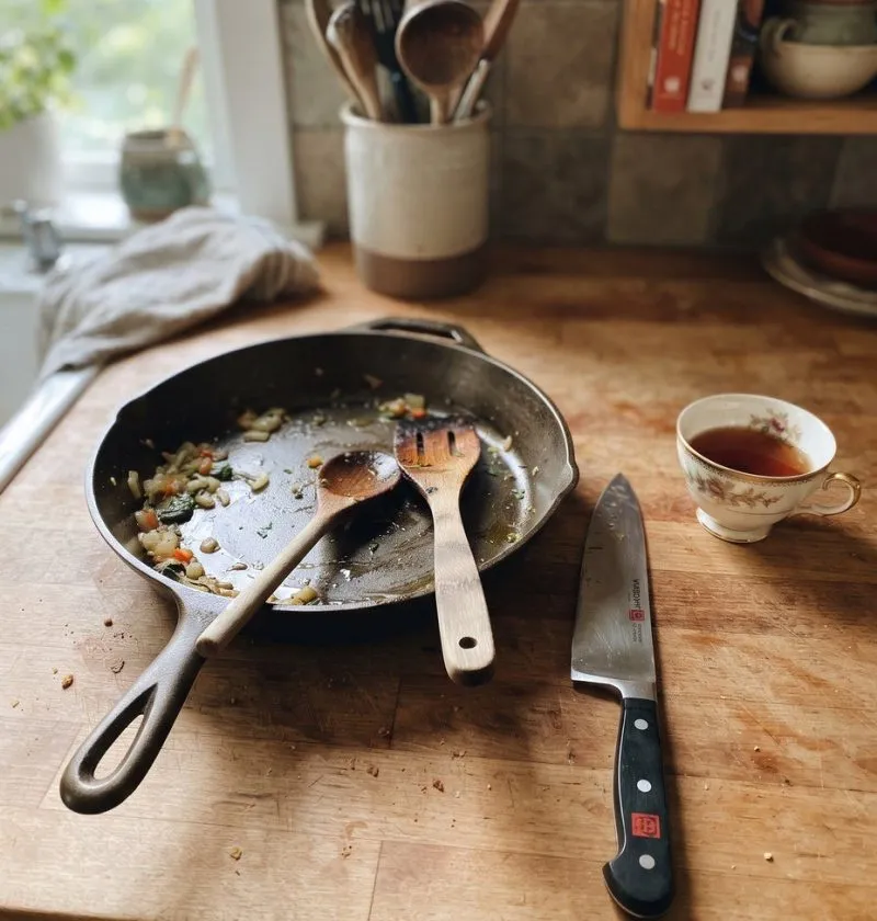 A cast iron skillet, wooden spoons, a knife and a china cup